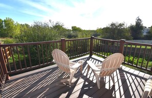 Una terraza de madera con dos sillas Adirondack orientadas a un exuberante paisaje verde.