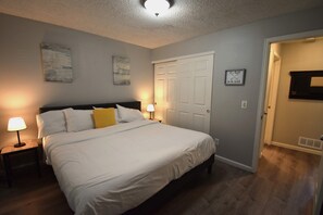 A bedroom with a bed, two bedside lamps, a door, and a wall-mounted picture.