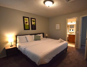 A hotel room with a bed, a nightstand, a lamp, and a bathroom visible through an open door. - Large Home in Aurora with Reservoir View (Aurora)