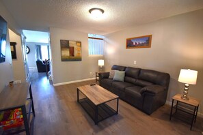 A living room with a leather sofa, a coffee table, a TV stand, and a painting on the wall. - Large Home in Aurora with Reservoir View (Aurora)