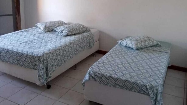 A room with two beds, each with patterned bedding, a ceiling fan, and two wall-mounted artworks. - Acalanto praia  (Peruibe)