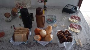 A table with various food items including bread, pastries, and a thermos. - Acalanto praia  (Peruibe)