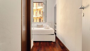 A narrow hallway leading to a bedroom with a bed, a window, and a view of a building. - JOIVY Cosy flat access to city centre (Milan)