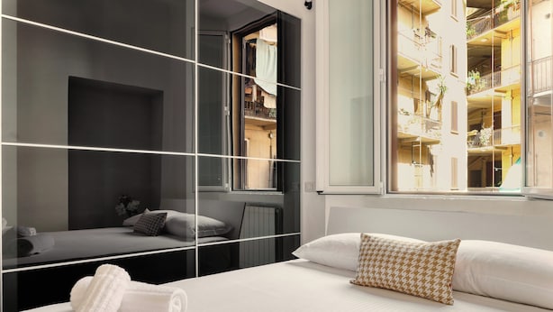 A modern hotel room with a large bed, a glass partition, and a view of the building's interior balconies. - JOIVY Cosy flat access to city centre (Milan)