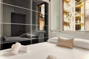 A modern hotel room with a large bed, a glass partition, and a view of the building's interior balconies. - JOIVY Cosy flat access to city centre (Milan)