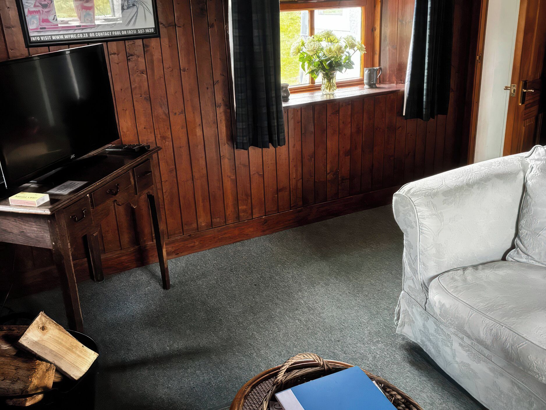 A room with a television on a wooden desk, a white sofa, a window with curtains, and a plant on the windowsill.