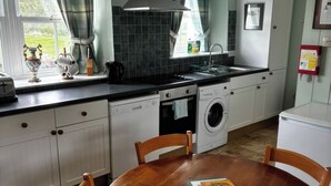 A kitchen with a dishwasher, washing machine, and a dining table with chairs. - Strathnoon (Inverness)