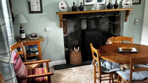 A cozy dining area with a wooden table and chairs, a fireplace, and a shelf with decorative items. - Strathnoon (Inverness)
