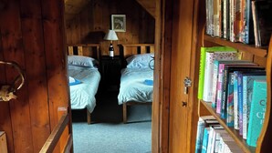 A wooden room with two beds, a bookshelf, and a door leading to another room. - Strathnoon (Inverness)