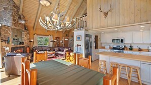 Amplia sala de estar con chimenea, una mesa de comedor con sillas de madera y una cocina con alacenas blancas y electrodomésticos de acero inoxidable.
