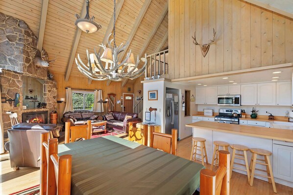A spacious living area with a fireplace, a dining table with wooden chairs, and a kitchen with white cabinets and stainless steel appliances.