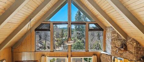 Une pièce aux hauts plafonds, avec des poutres en bois, de grandes fenêtres, une cheminée en pierre et un lustre.