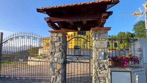 Una entrada protegida con pilares de piedra y un portón de metal, que conduce a un edificio con fachada amarilla y techo rojo.