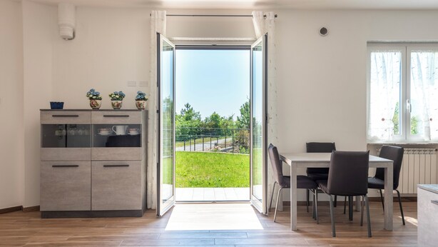 Una cocina moderna con comedor, una puerta corrediza de vidrio que da a un balcón y vistas a zonas verdes.