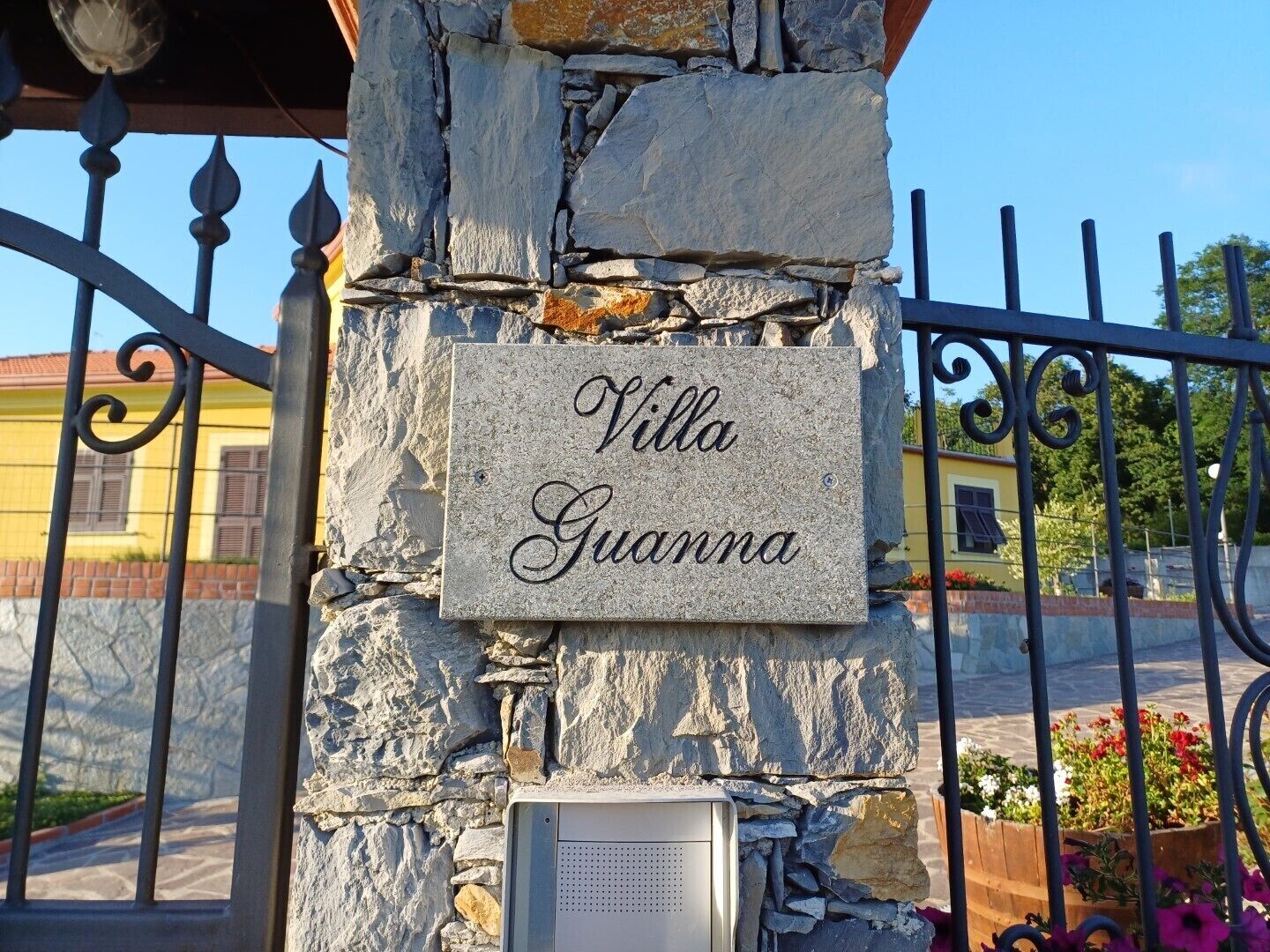 A stone wall with a sign that reads "Villa Guanna" and a metal gate.