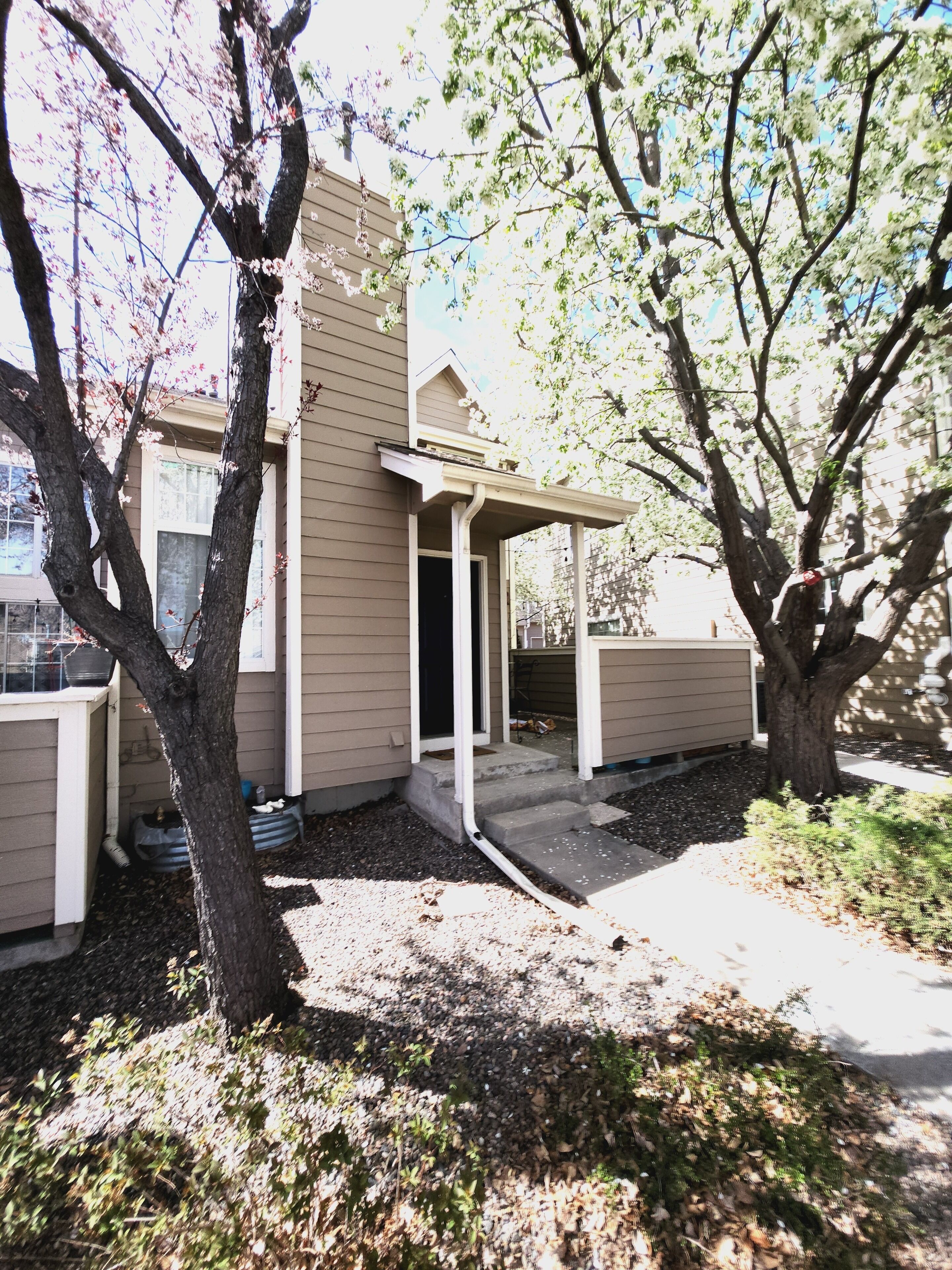 A two-story house with a covered porch, a front door, and a small front yard with trees and a gravel path.