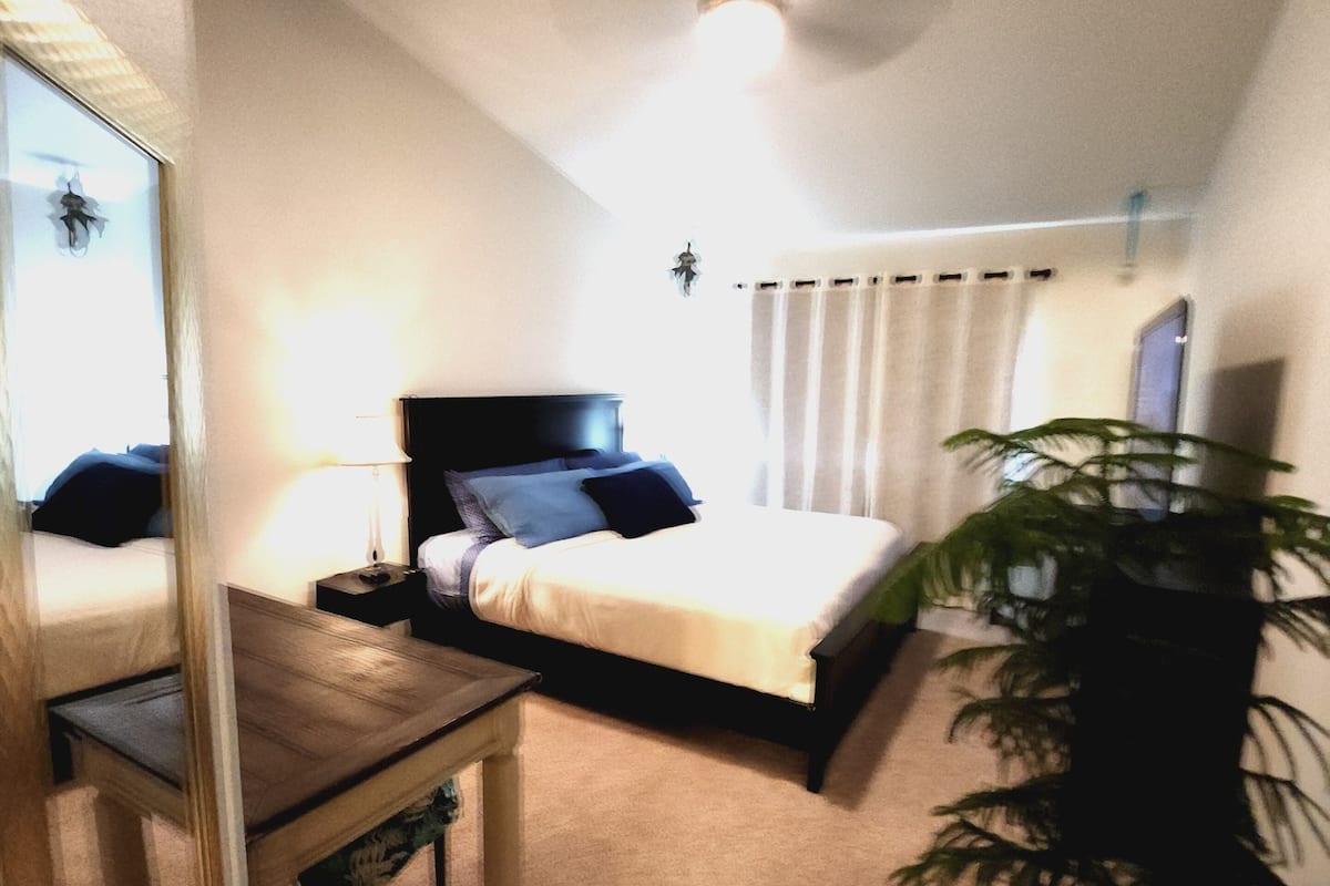 A bedroom with a bed, bedside table, lamp, and a mirror.