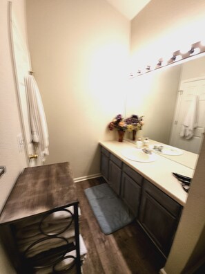 A compact bathroom with a wooden vanity, a small sink, and a mirror. There is a towel rack on the wall and a small rug on the floor. - Casa de gato (Westminster)
