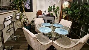 A dining area with a glass table, four chairs, a chandelier, and potted plants. - Casa de gato (Westminster)