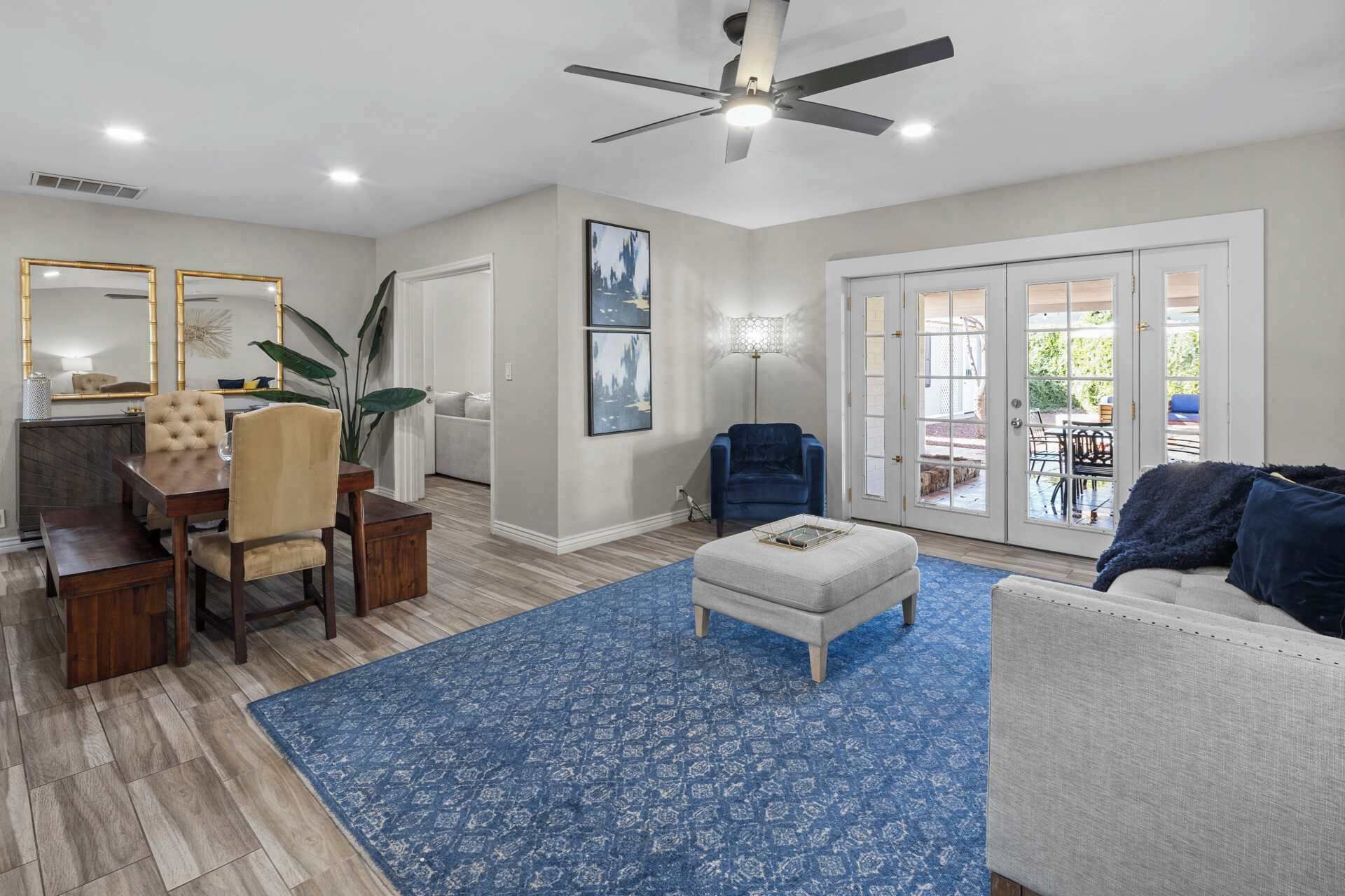 A spacious living room with a ceiling fan, a dining area with a wooden table and chairs, and a large window with a view of the outdoors.