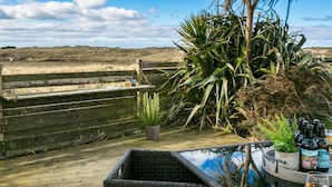 A wooden deck with a grill, potted plants, and bottles of beverages. - Pen Tywyn - sleeps 7 guests  in 3 bedrooms (Rhosneigr)