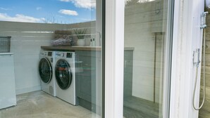 A laundry area with two front-loading washing machines, a drying rack, and a shower area with a hose. - Pen Tywyn - sleeps 7 guests  in 3 bedrooms (Rhosneigr)