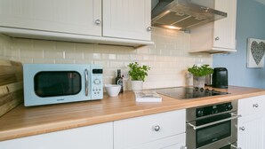 A modern kitchen with white cabinetry, a light blue microwave, a gas stove, and two ovens. - Pen Tywyn - sleeps 7 guests  in 3 bedrooms (Rhosneigr)