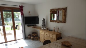 A dining area with a wooden table and chairs, a television mounted on the wall, a cabinet with decorative items, and a patterned rug on the floor. - Semi-detached house, 3* 5 beds, 2 bedrooms garage parking, enclosed garden, WIFI (Bolquère)