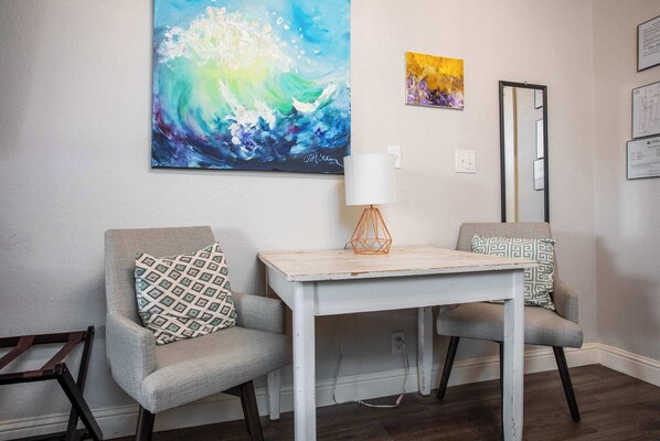 A room with two armchairs, a small table, a large abstract painting, and a mirror on the wall.