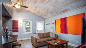 A living room with a wooden ceiling, a brown sofa, a coffee table, and a large abstract painting on the wall.