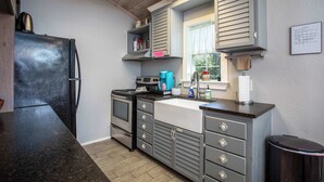 A compact kitchen with a black refrigerator, a stove, and a sink. There are cabinets with decorative handles and a window with blinds.