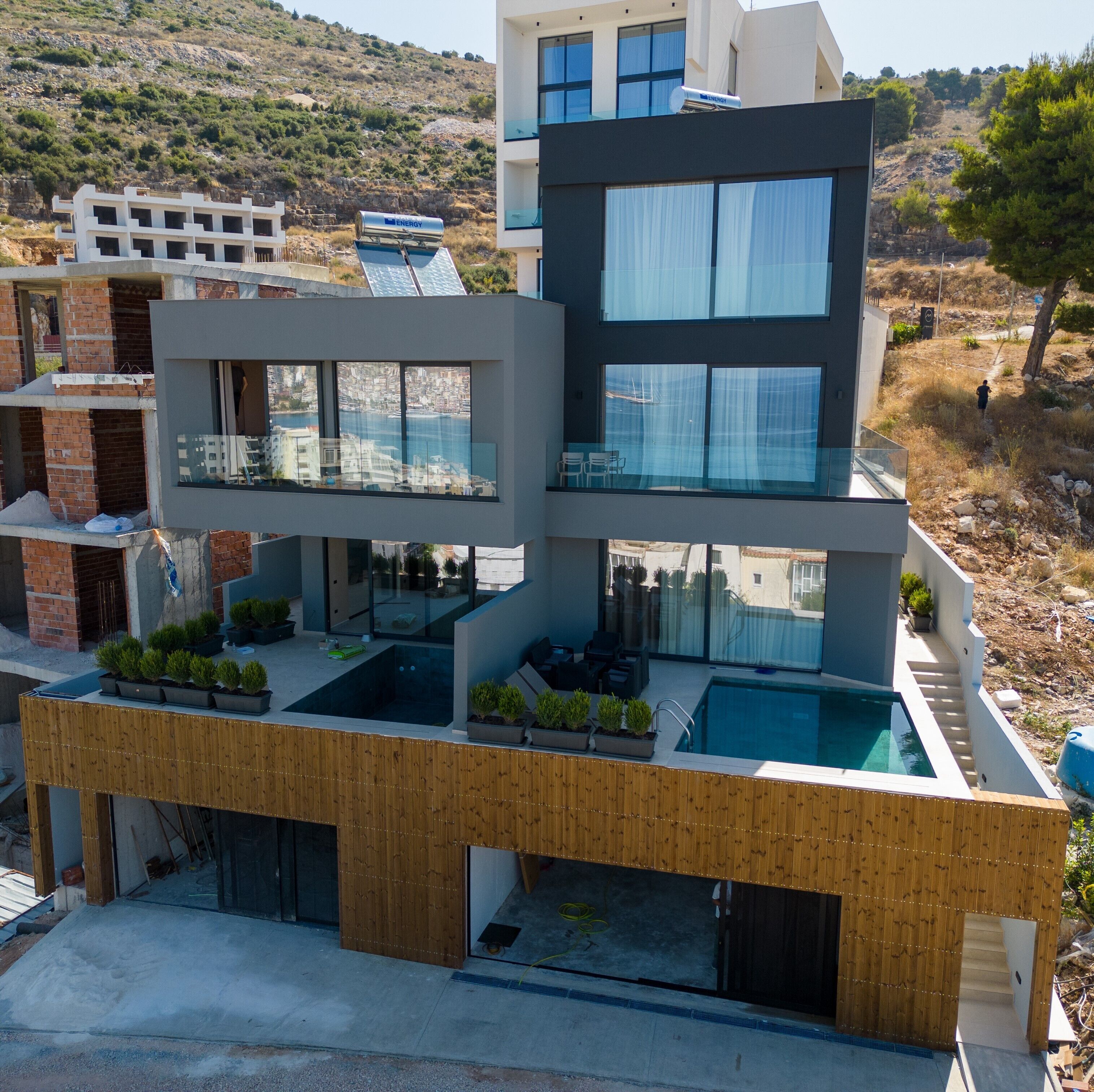 A modern multi-story building with a rooftop pool, large windows, and a view of the surrounding landscape.