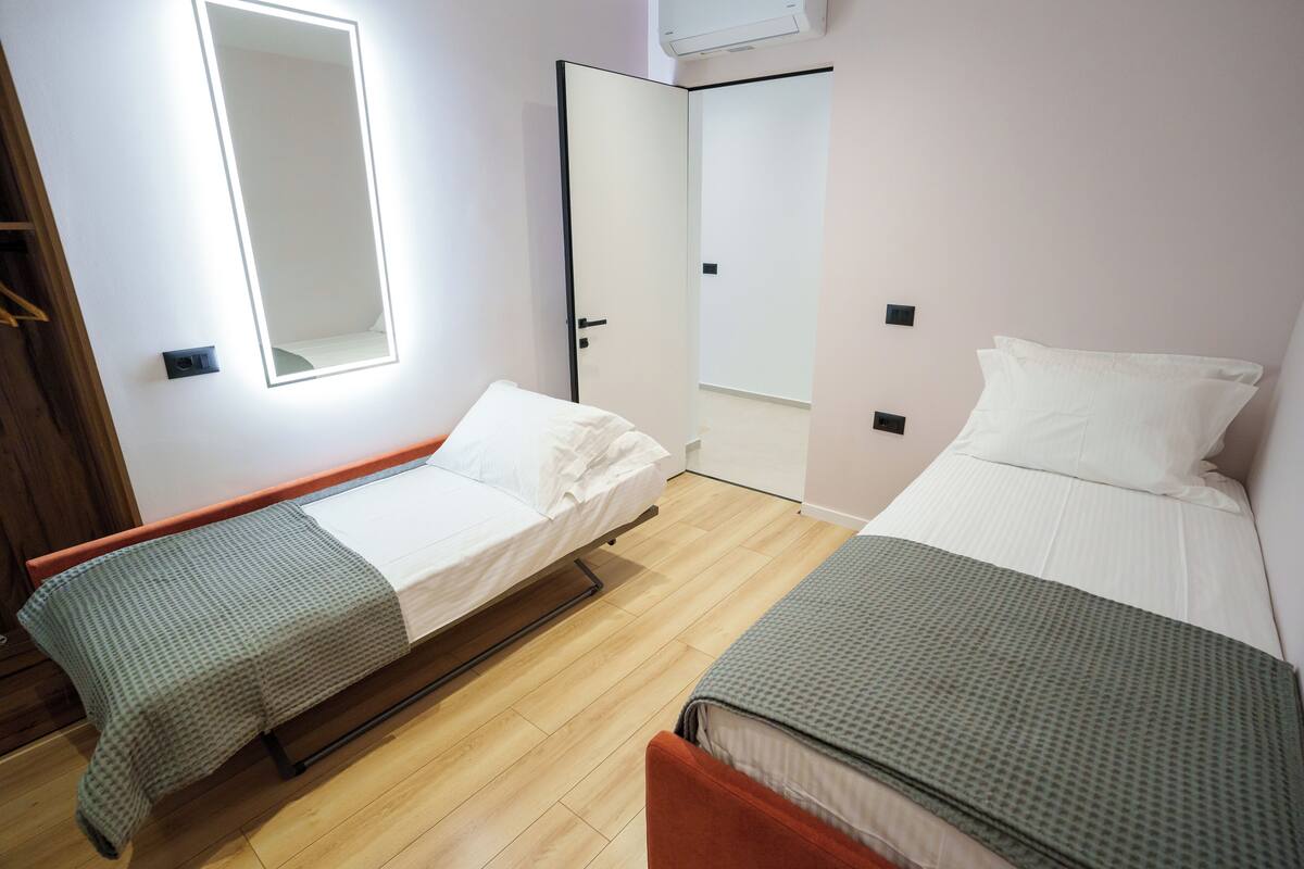 A bedroom with two single beds, a wooden floor, a mirror, and a wardrobe.