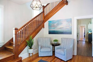 A staircase with wooden railings leading to a landing area. There is a painting on the wall above the staircase, a small round table with a plant, and two grey armchairs. - Chesapeake Charm Estate, Two Blocks from the Beach (Cape Charles)
