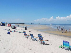 A beach with rows of beach chairs, a few tents, and a lighthouse in the distance. - Chesapeake Charm Estate, Two Blocks from the Beach (Cape Charles)