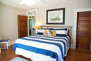 A bedroom with a large bed, a nightstand with a lamp, a framed picture on the wall, and wooden doors.