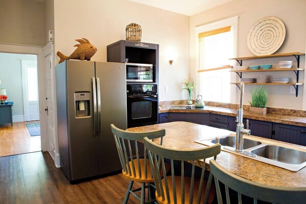 A modern kitchen with a built-in refrigerator, oven, and microwave. There is a dining area with two chairs and a kitchen island with a sink.