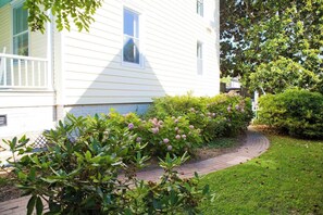 A white house with a brick pathway leading to a well-maintained garden with hydrangea bushes.