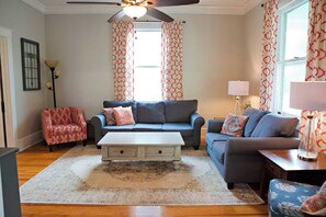 A living room with a blue sofa, a red patterned armchair, a white coffee table, and a patterned rug. - Chesapeake Charm Estate, Two Blocks from the Beach (Cape Charles)