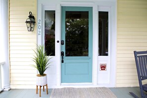 A front door with a number '202' above it, a potted plant, and a chair on the porch.