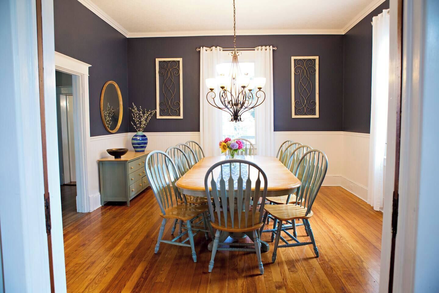A dining room with a wooden table and six chairs, a chandelier, and decorative wall art.