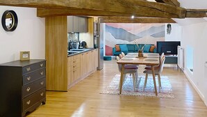 Un ampio loft con travi a vista in legno, una cucina con elettrodomestici moderni, un'area pranzo con tavolo e sedie, e un accogliente soggiorno con divano e TV.