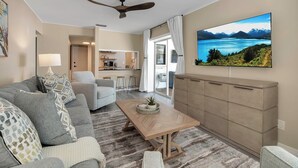 A living room with a sofa, a coffee table, and a TV displaying a mountain landscape.