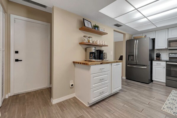 A modern kitchen with white cabinets, stainless steel appliances, and wooden shelves. - Charming 3-BR Home Near AMI~ Heated Pool, Spa, Game Room, Putt-Putt, Basketball (Bradenton)