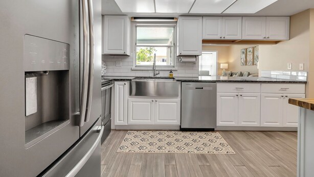 A modern kitchen with white cabinets, stainless steel appliances, and a patterned rug.