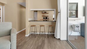 A modern kitchen with a bar stool seating area, a built-in coffee station, and a sliding glass door leading to a balcony.