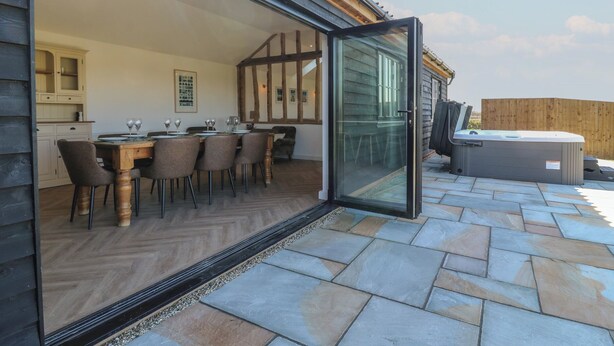 An open patio with a dining area, a hot tub, and a view of the surrounding landscape. - The Hide (Colchester)