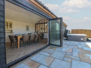 An open patio with a dining area, a hot tub, and a view of the surrounding landscape. - The Hide (Colchester)