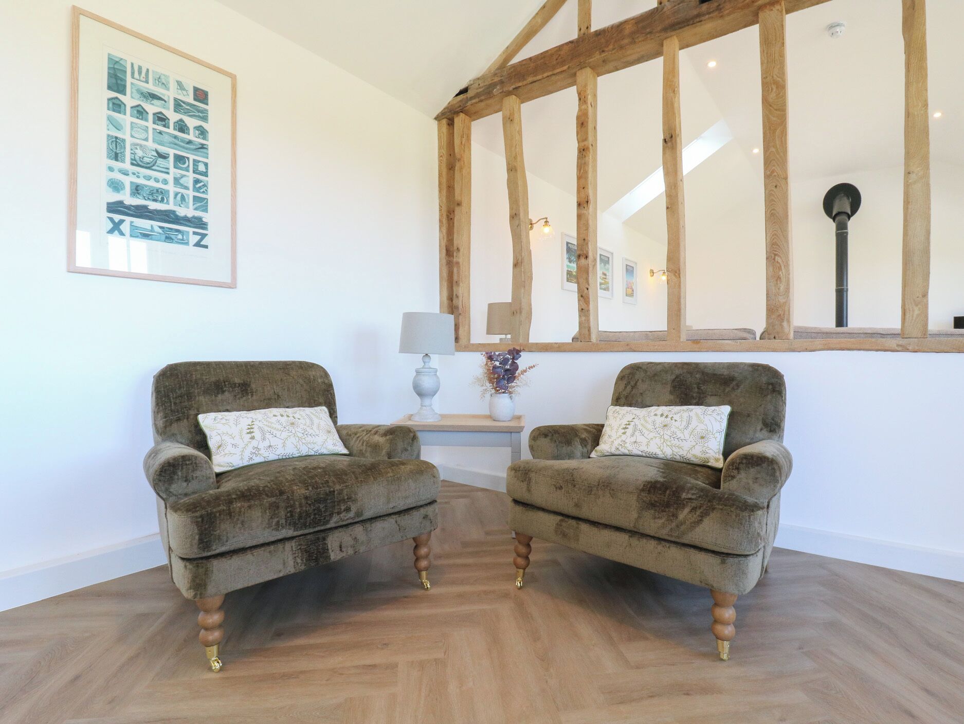 Una stanza con due poltrone, travi a vista in legno, un quadro incorniciato, una lampada e un vaso con fiori secchi.