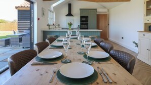 A dining area with a long wooden table set for six, equipped with plates, cutlery, and wine glasses. - The Hide (Colchester)